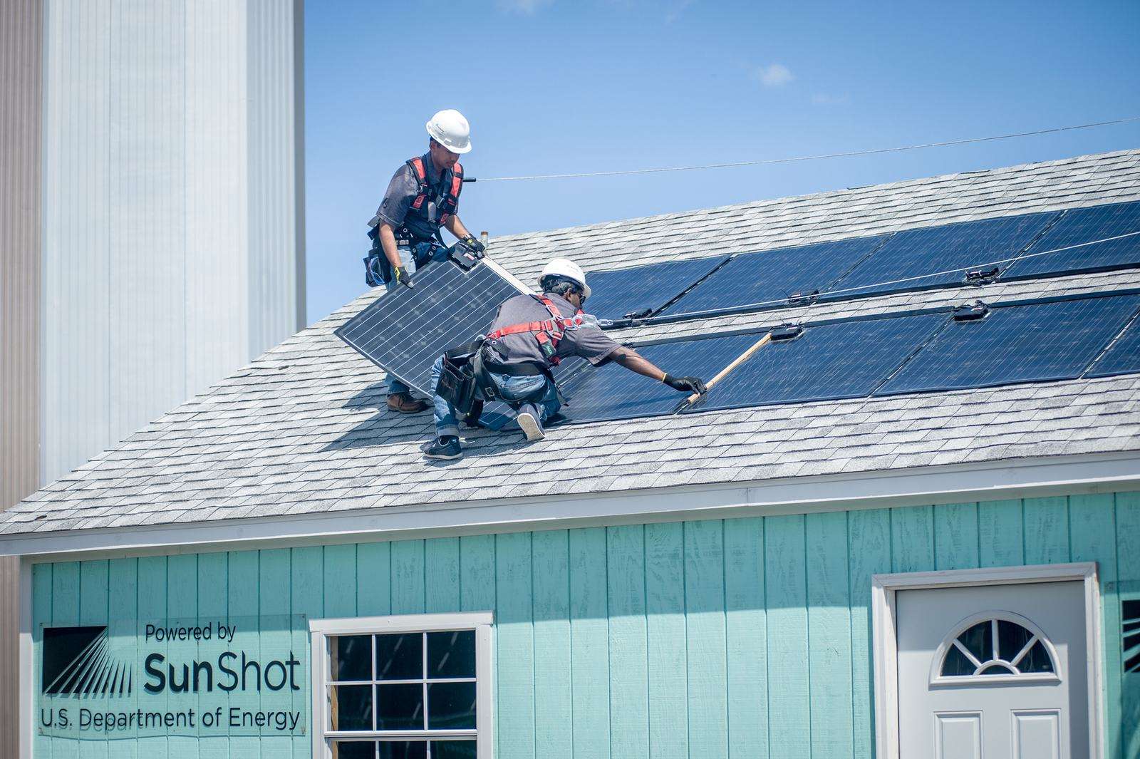 Two installers placing solar panels on a house roof