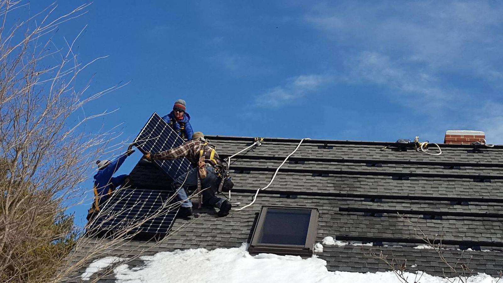 Installer mounting solar panels on a roof in winter