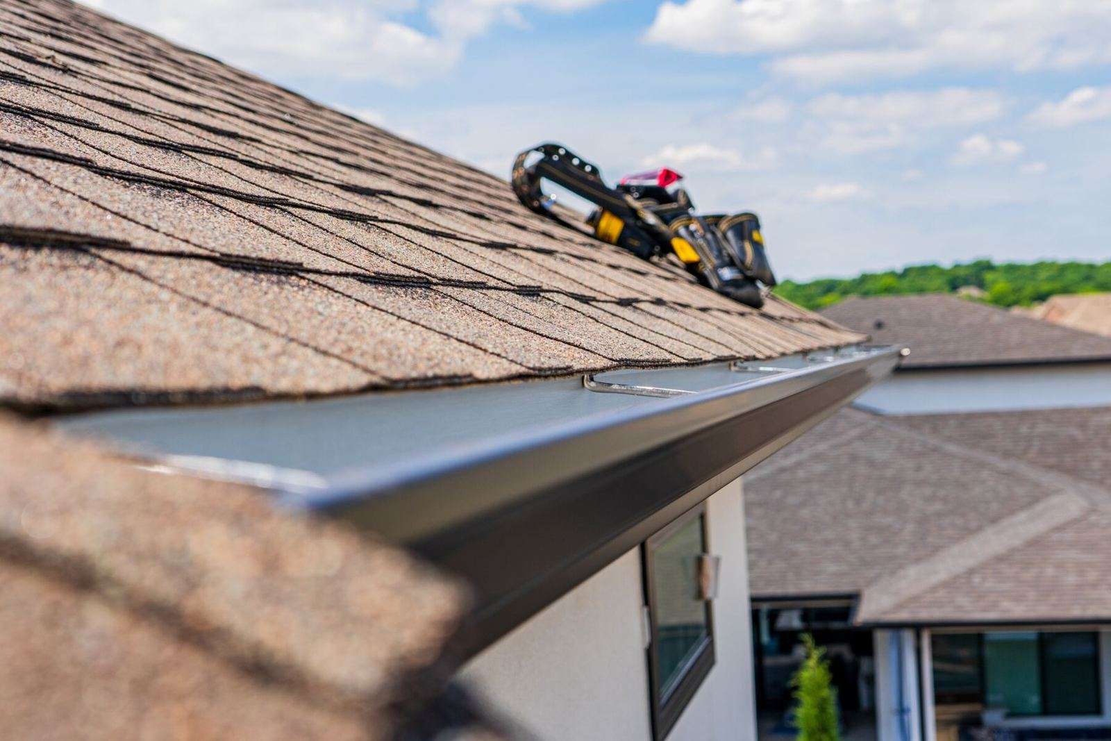 Seamless gutter being installed along a shingle roof edge