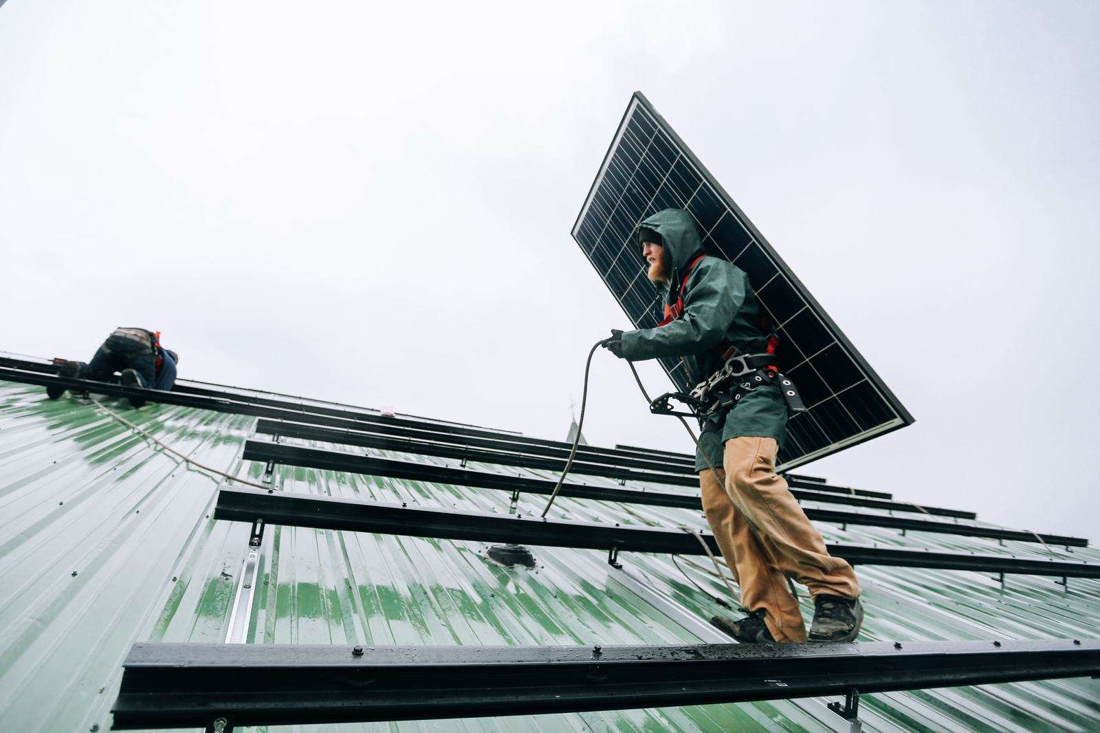 Technician carrying a solar panel across a metal roof